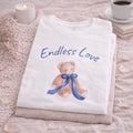 Folded white shirt with teddy bear and 'Endless Love' text on a textured surface.