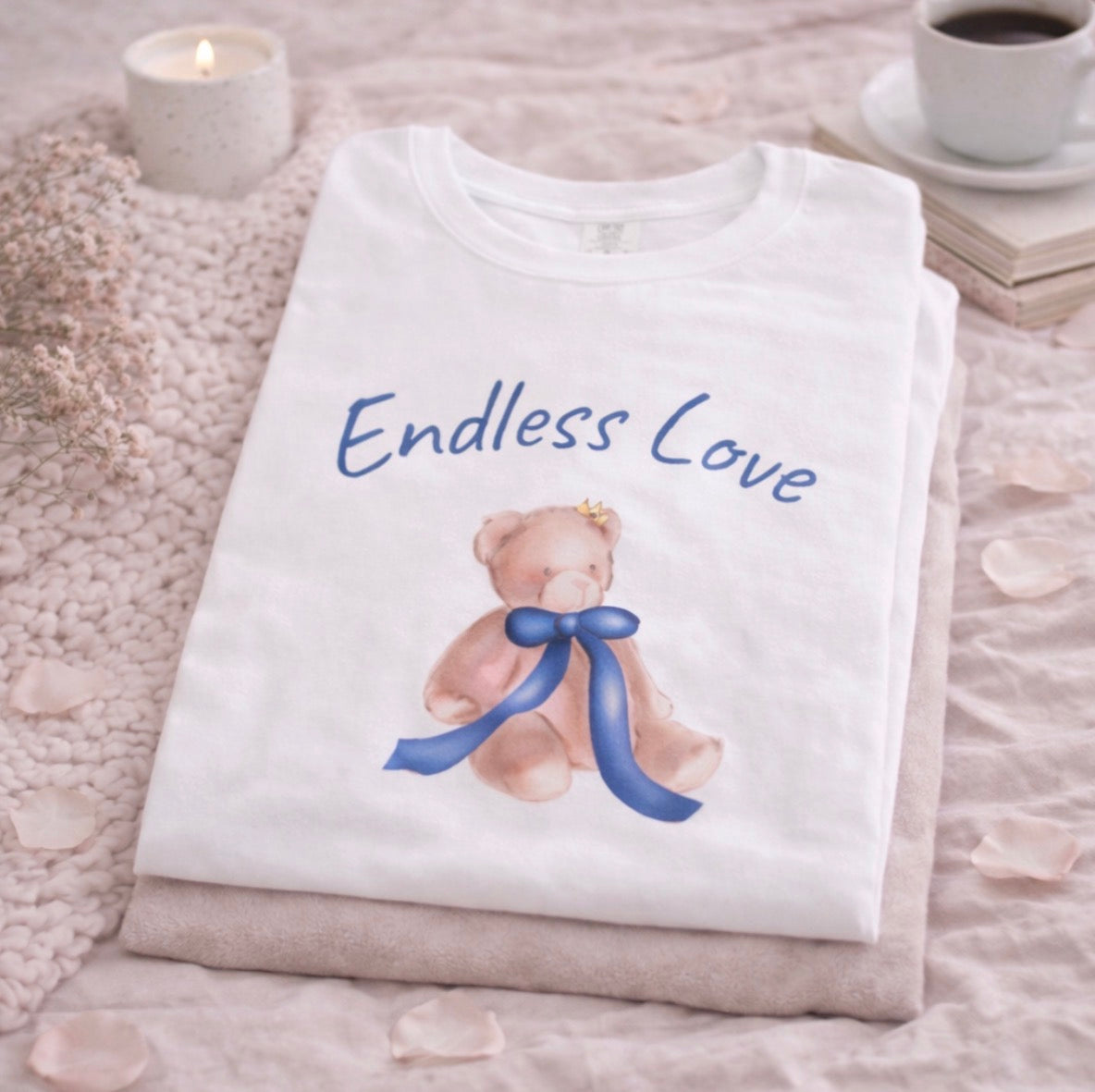 Folded white shirt with teddy bear and 'Endless Love' text on a textured surface.