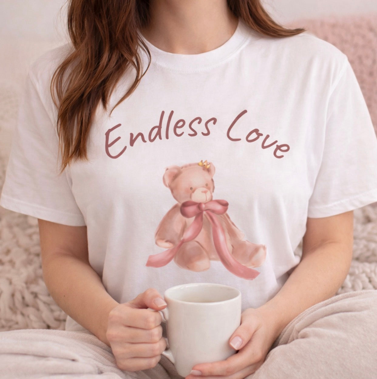 Person wearing a white t-shirt with a teddy bear and 'Endless Love' text, holding a mug.